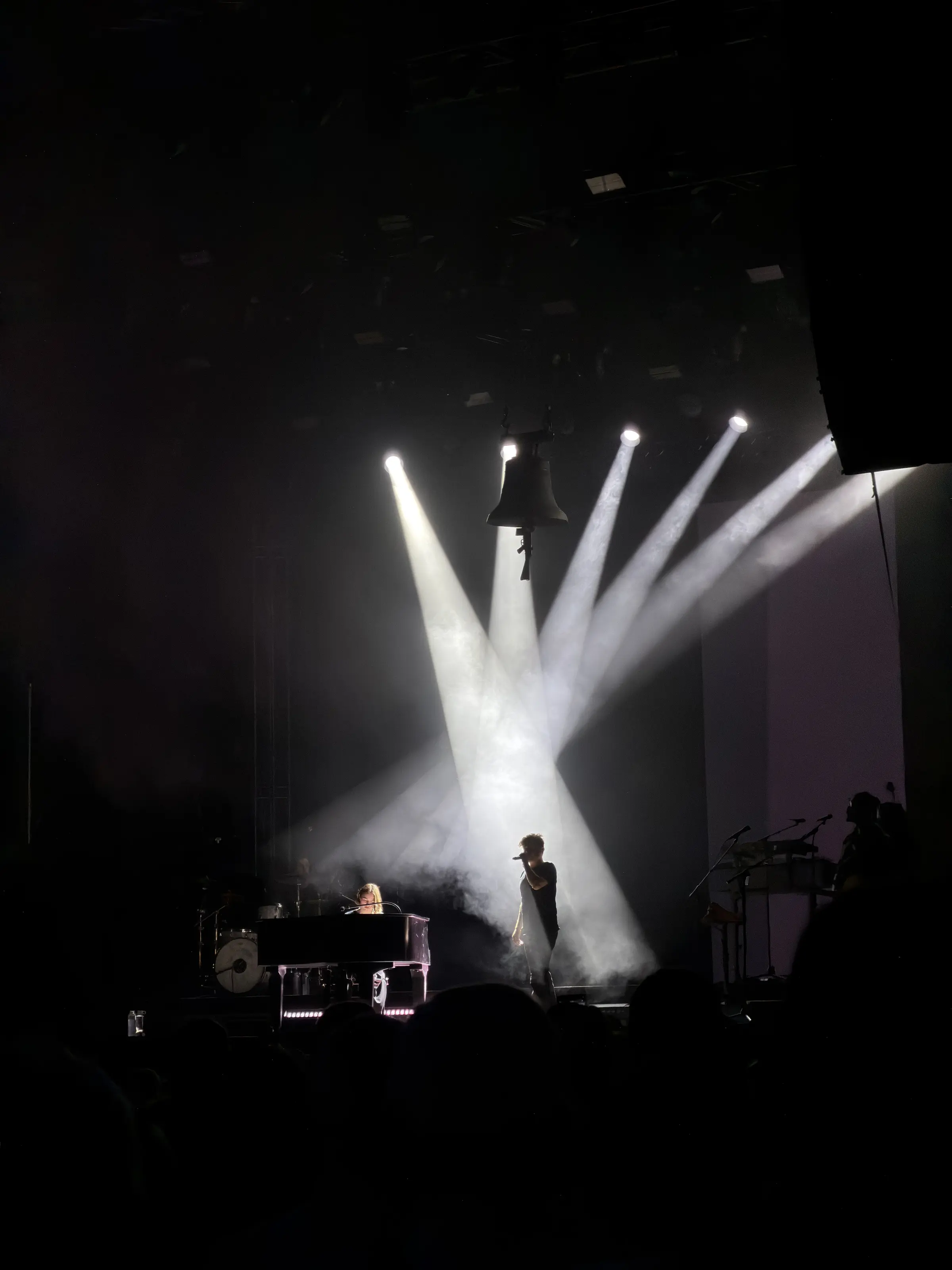 Konzertszene mit Glocke, Lichtkegeln, Klavier und Künstler