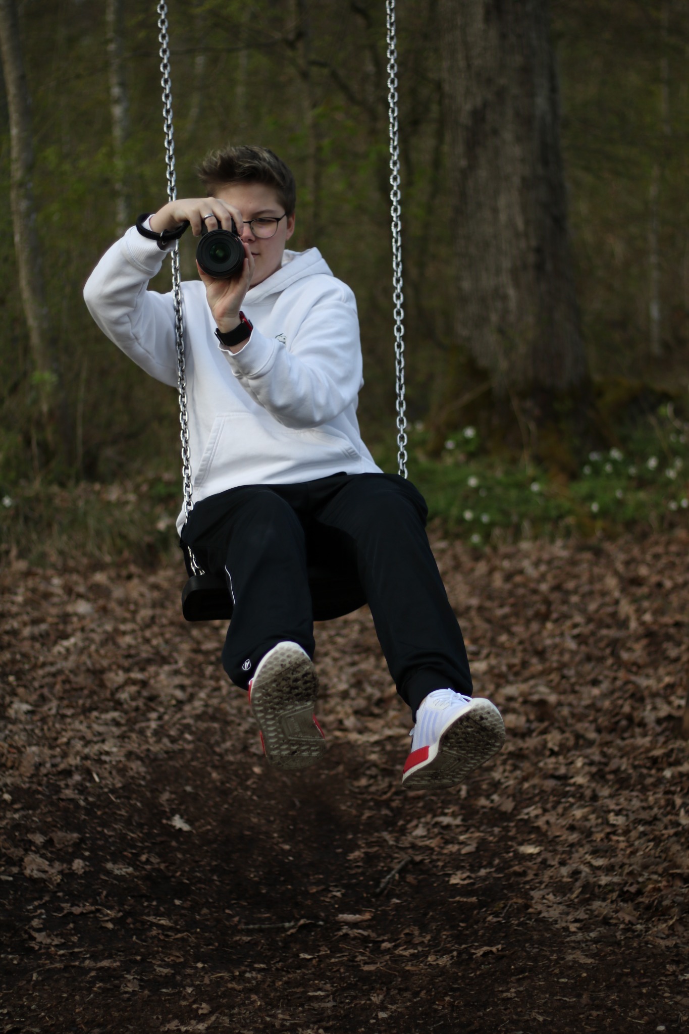 Millane Ullmann sitzt mit ihrer Kamera auf einer Schaukel im Wald