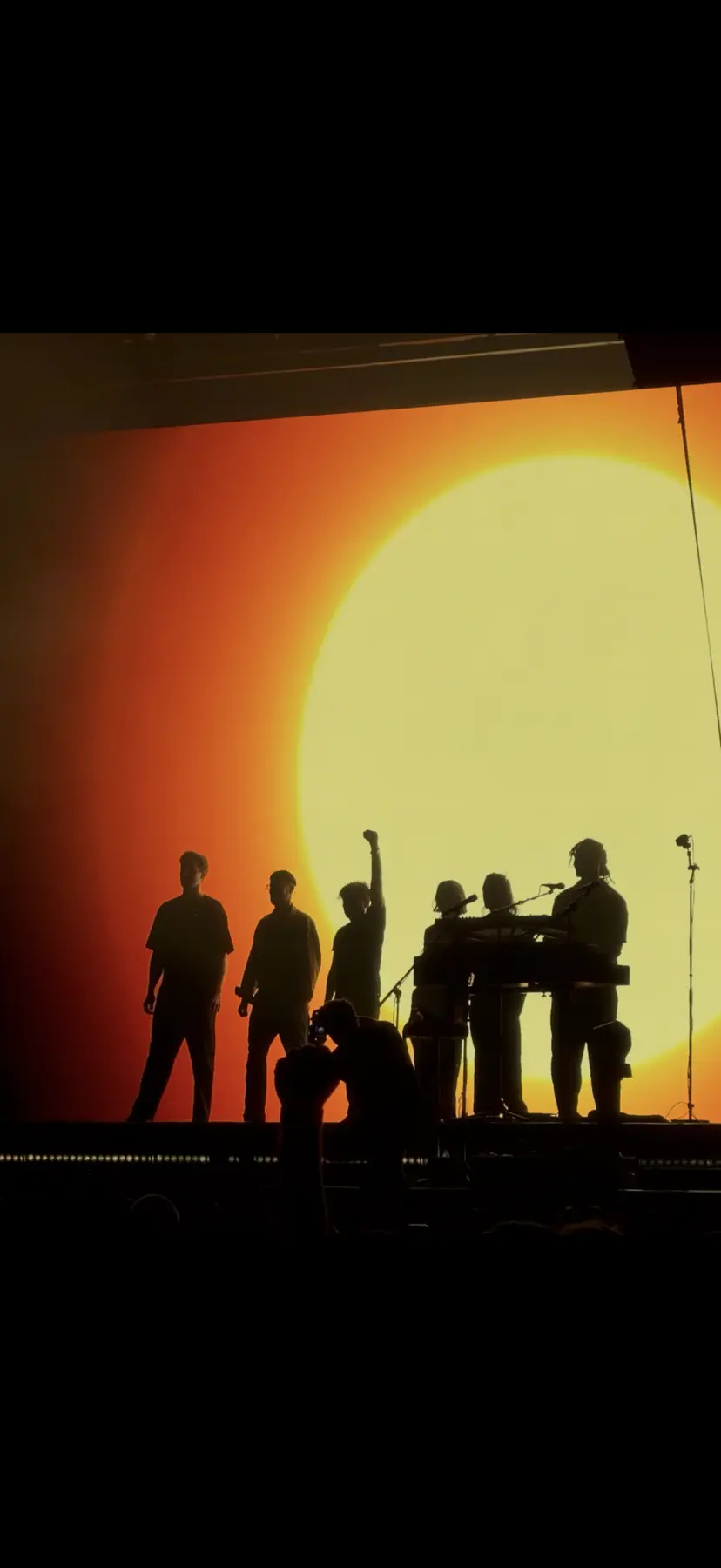 Silhouetten einer Band vor einer orangefarbenen Sonne